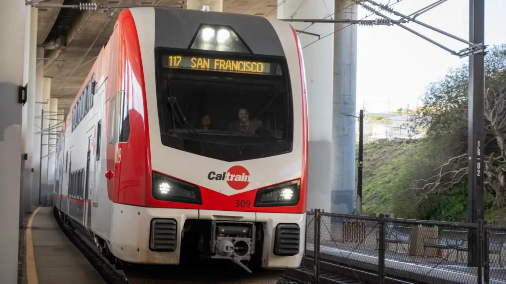 A Caltrain, which is white and red, on the tracks with a notice that it is heading to San Francisco