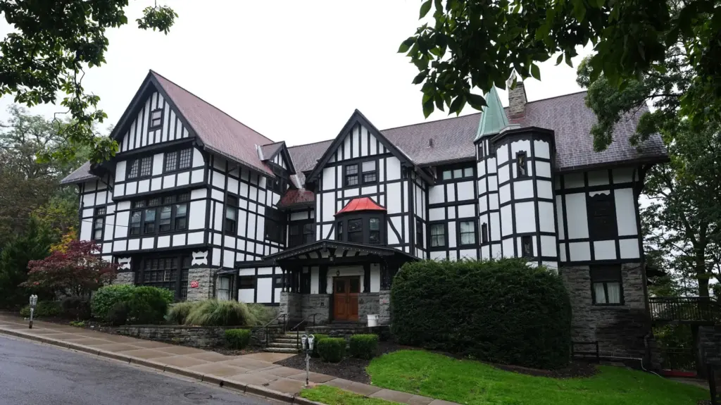 A large Tudor-style house set amid tall green trees.