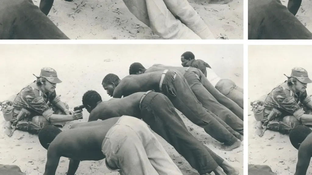 A white Rhodesian soldier points a gun at African villagers who are in a plank position during an interrogation.
