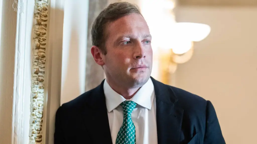 Photograph of Rep. Max Miller wearing a dark suit with a green tie